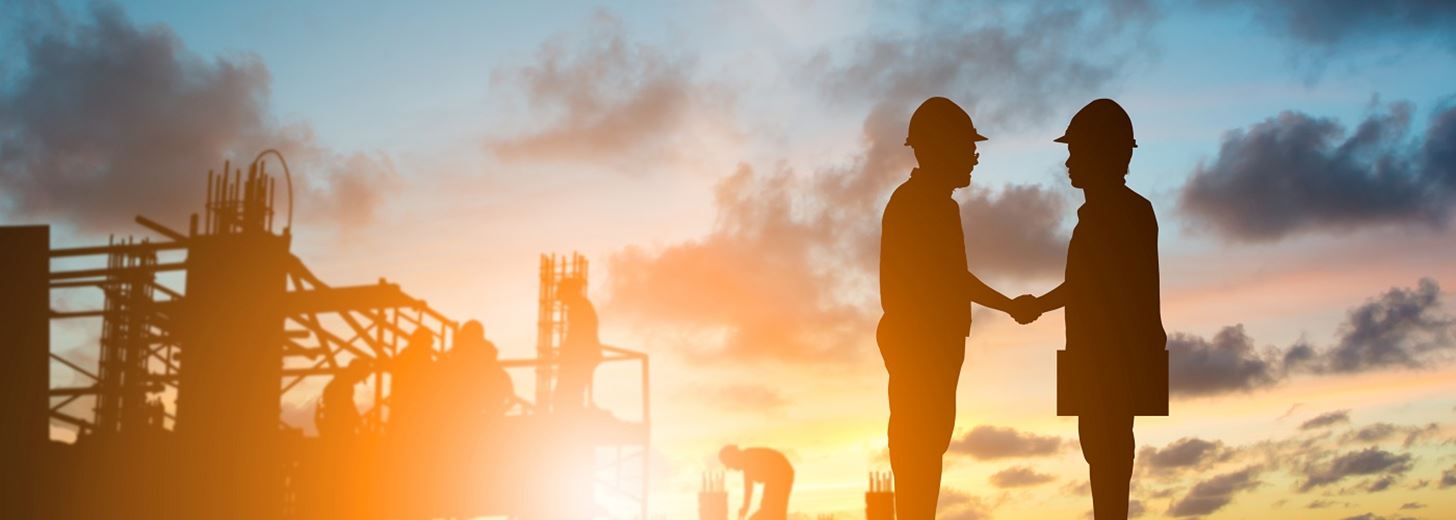 SILHOUETTE of builders on a construction site shaking hands in front of a sunset 